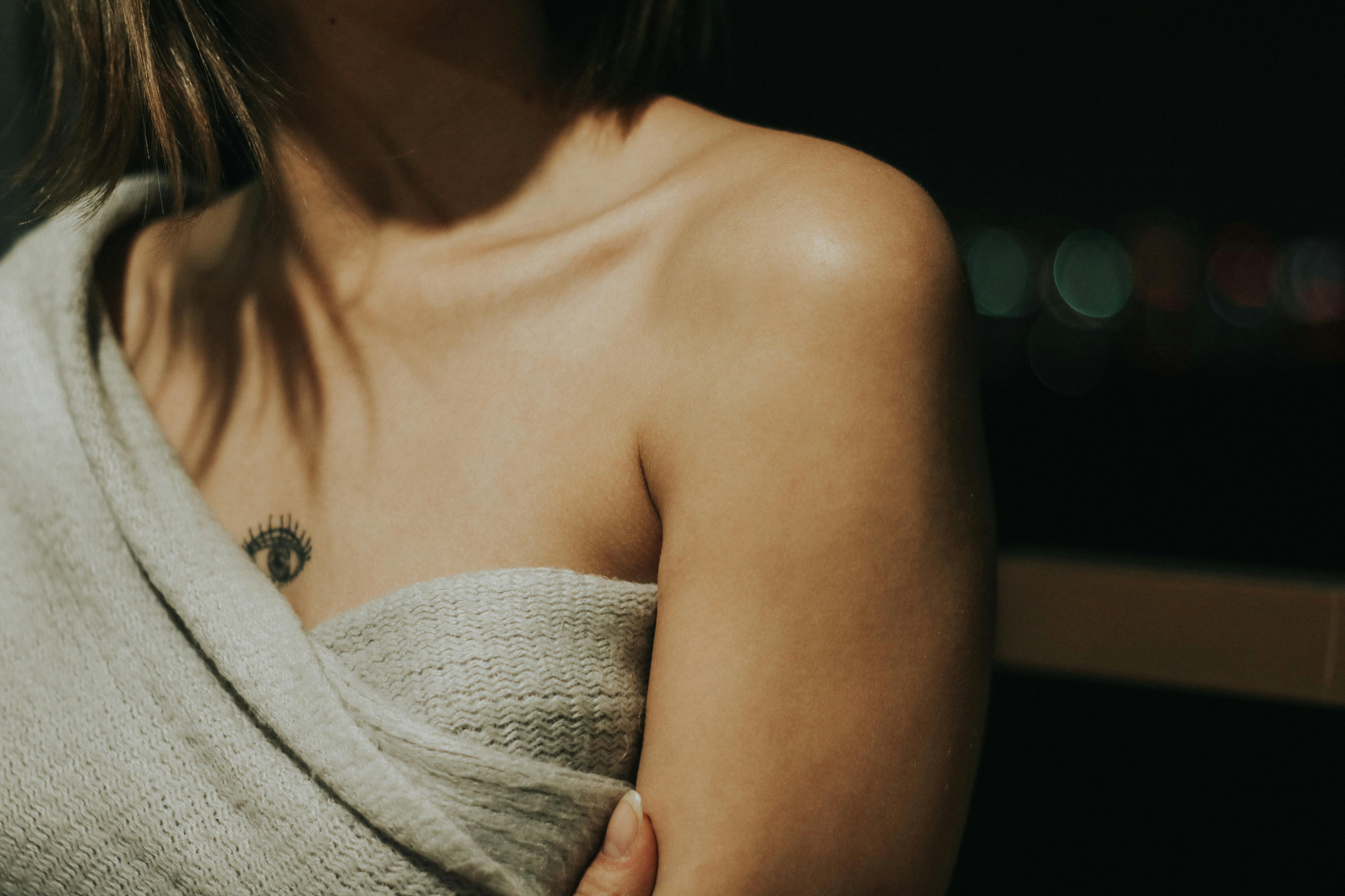Intimate close-up of a woman's shoulder and tattoo, draped in a cozy fabric.