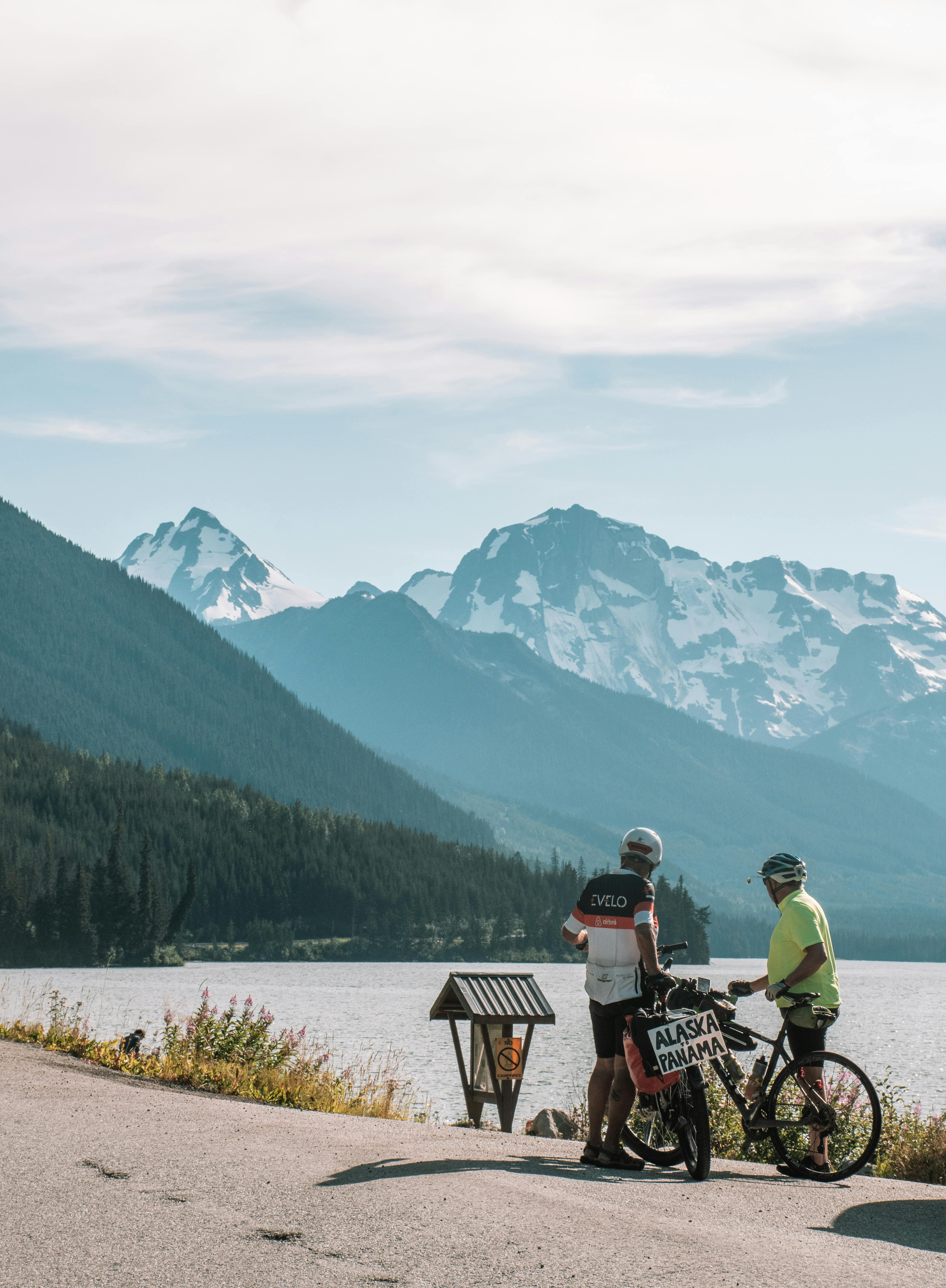 two people on bikes near a lake with mountains in the background