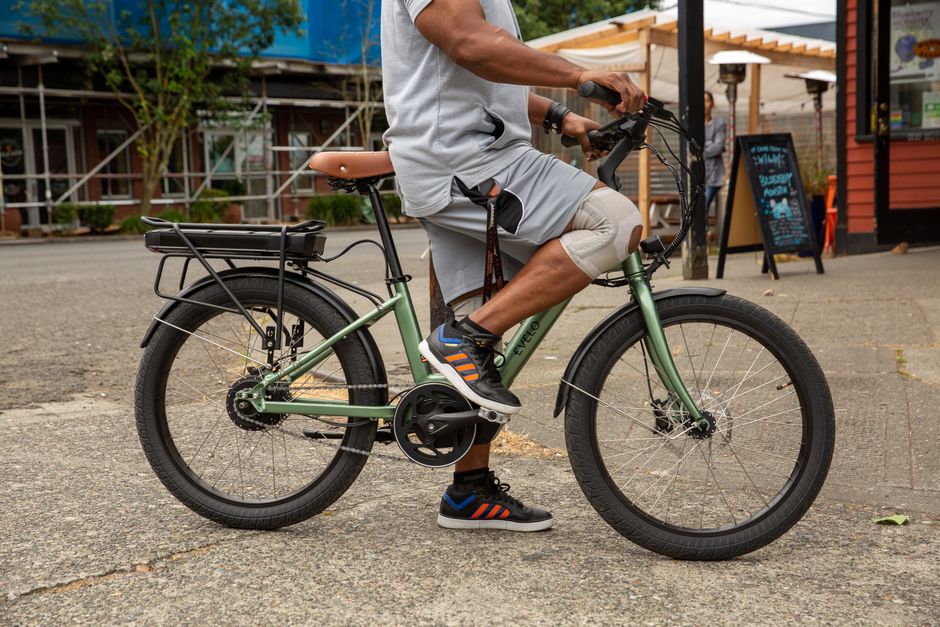 A man leisurely rides an electric bicycle on a city street, enjoying the outdoors.