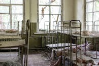 一间废弃的房间尘土飞扬，里面有破旧的金属床和破碎的窗户，处处显露出腐烂的迹象