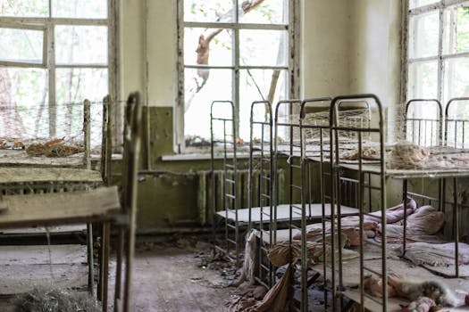 一间废弃的房间尘土飞扬，里面有破旧的金属床和破碎的窗户，处处显露出腐烂的迹象