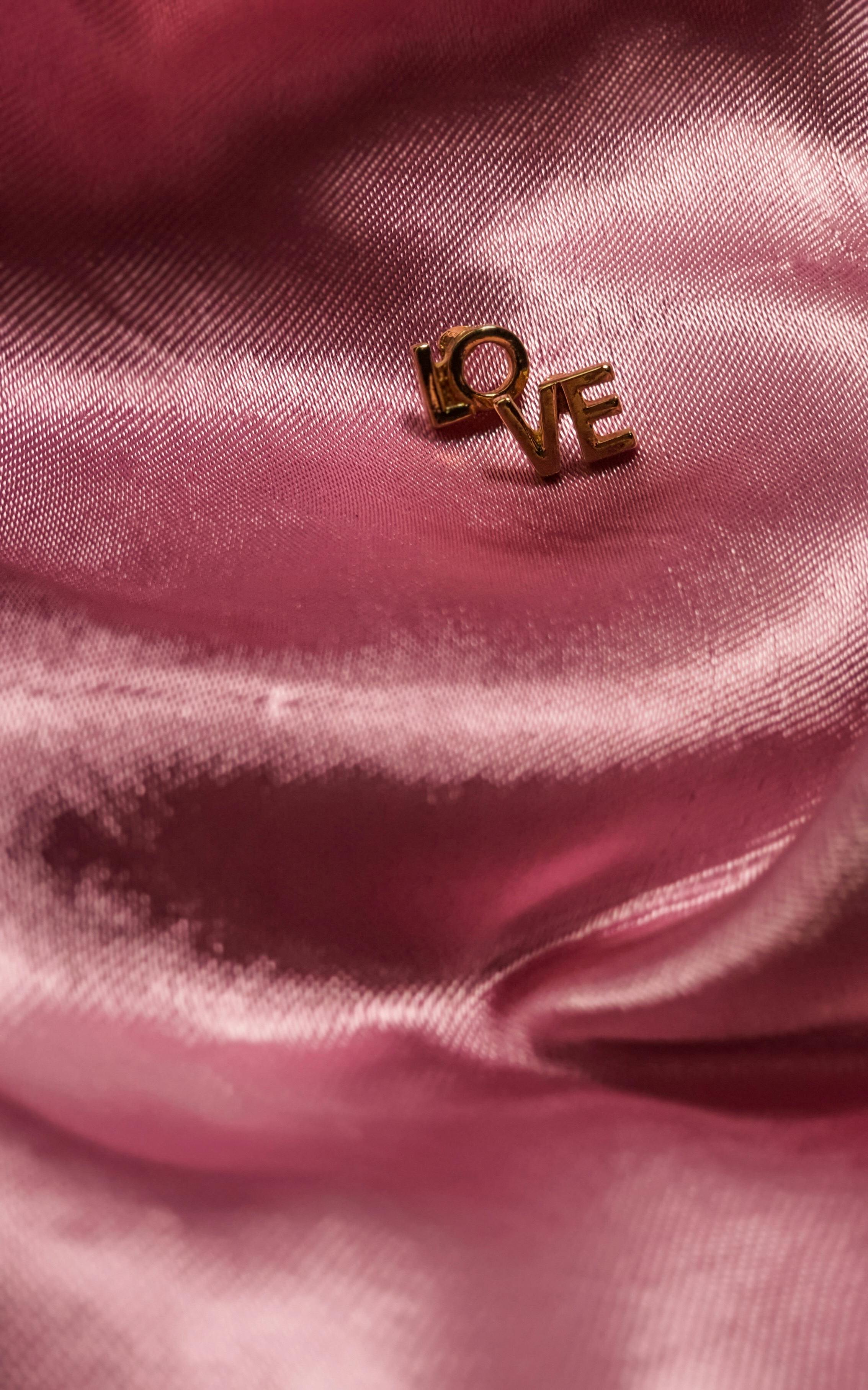 Elegant gold 'Love' earring on pink satin fabric, capturing a sense of romance and style.