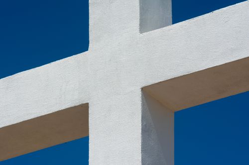 Free A minimalist white cross structure set against a bright blue sky, symbolizing purity and modern design. Stock Photo