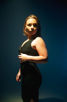 Glamorous studio portrait of a confident woman in a black dress with dramatic lighting.