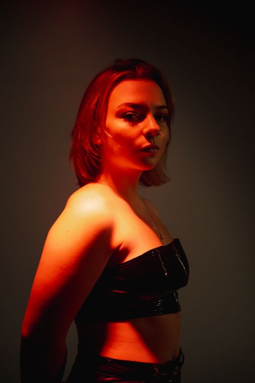 Free Fashion portrait of a woman in red light wearing black attire, showcasing bold and dramatic style. Stock Photo