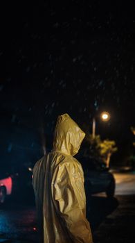 A person stands in a yellow raincoat under street lights on a rainy night.