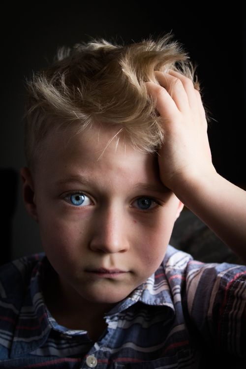 Free Close-up portrait of a child with blue eyes, hand on head, in studio lighting. Stock Photo