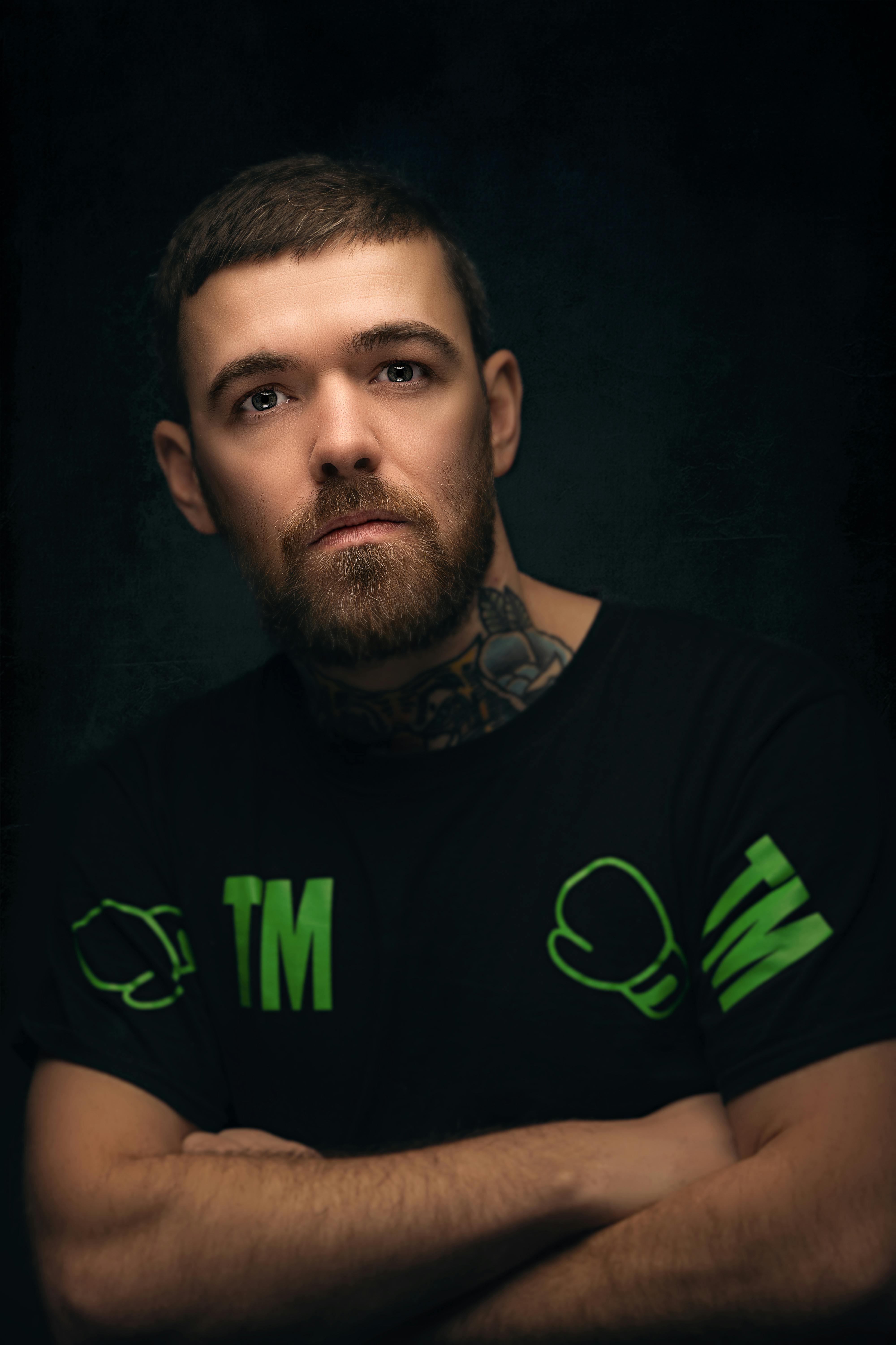 Portrait of a tattooed man with crossed arms against a black background.