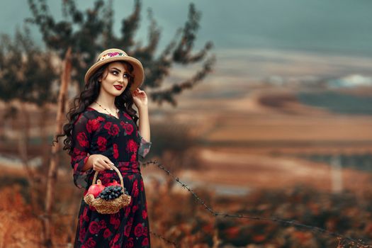 A stylish woman in a floral dress and hat holding a basket in Piranshahr, Iran.