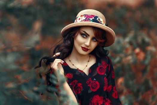 Woman in floral dress and hat posing outdoors with a vibrant, artistic background.