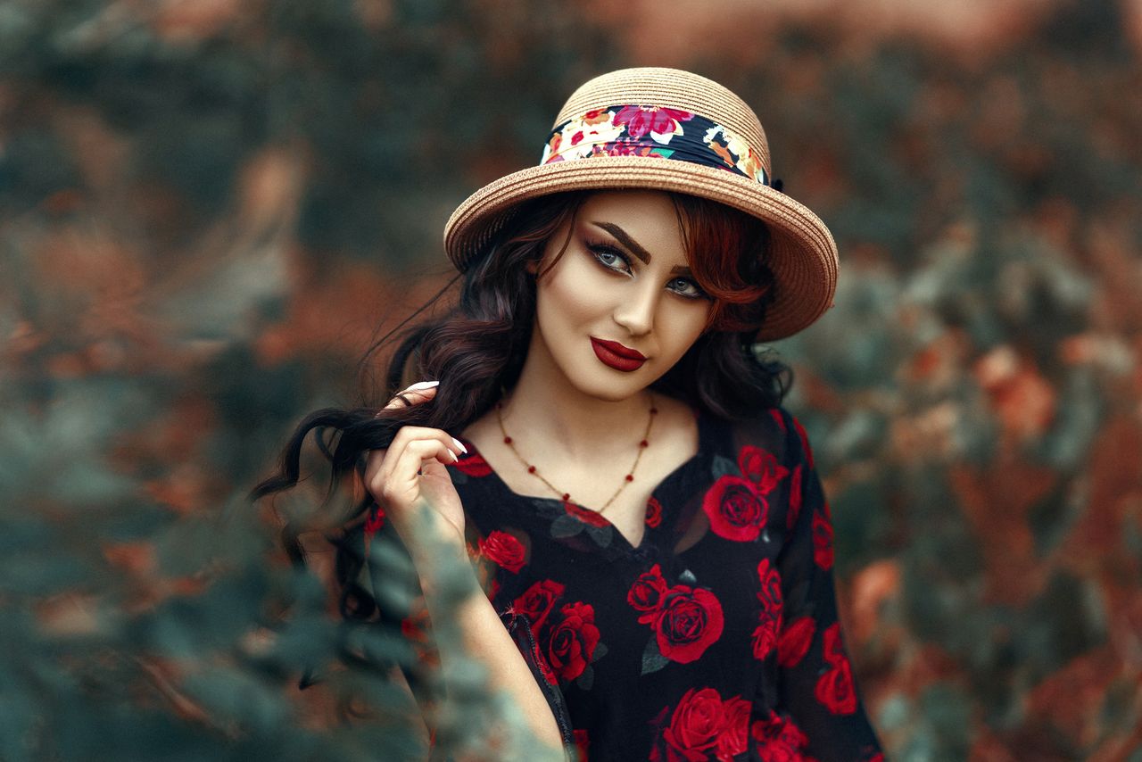 woman in floral dress and hat posing outdoors with a vibrant artistic