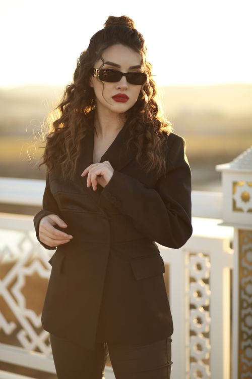 Free Sophisticated woman in a black jacket and sunglasses enjoying the sunlight outdoors. Stock Photo