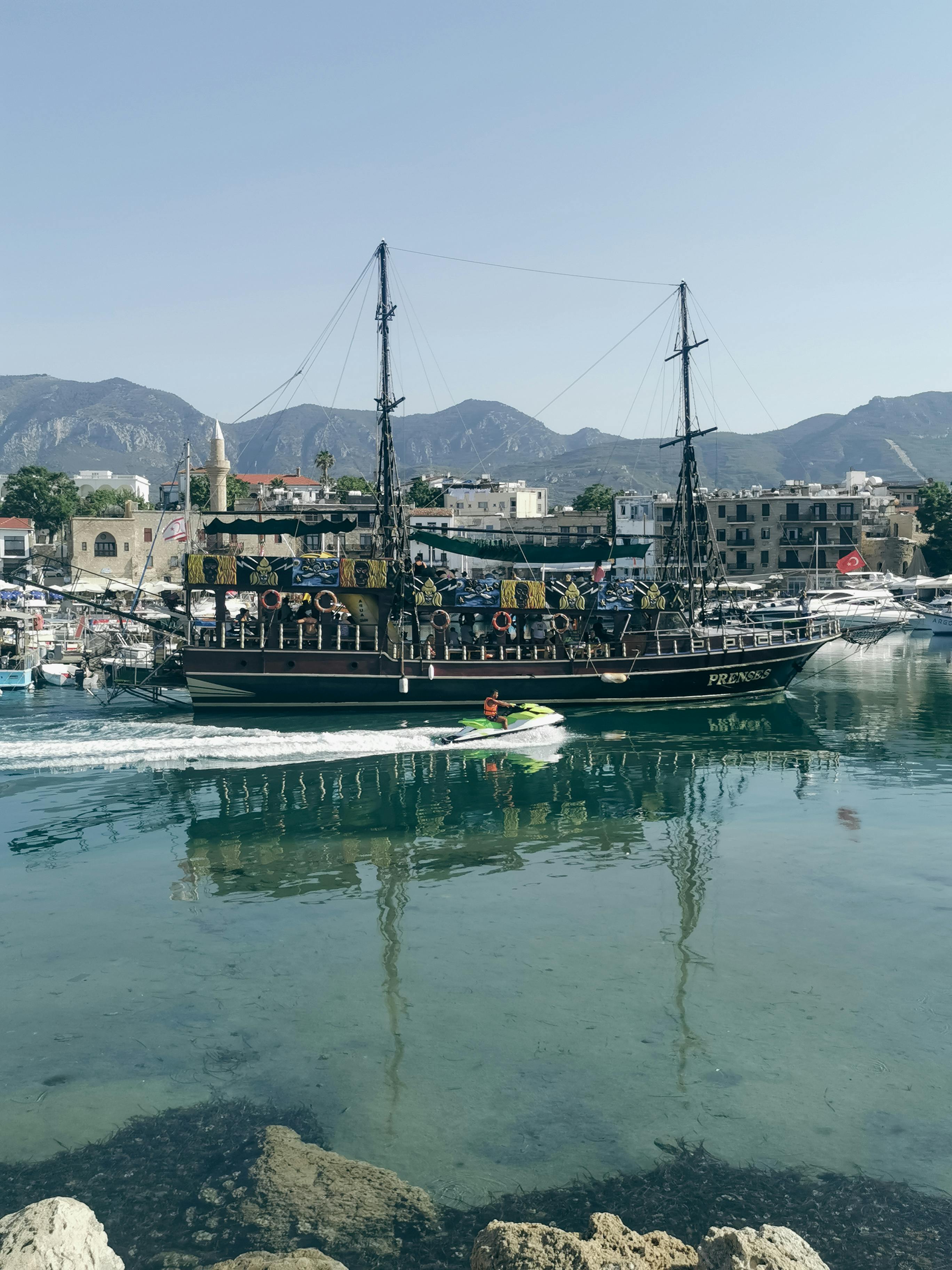 Prescription Goggle Inserts - A scenic view of a historic ship sailing in Girne Harbor, Cyprus, with mountains in the background.