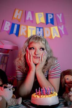 Joyful woman with tiara celebrating birthday with cake and colorful banner.