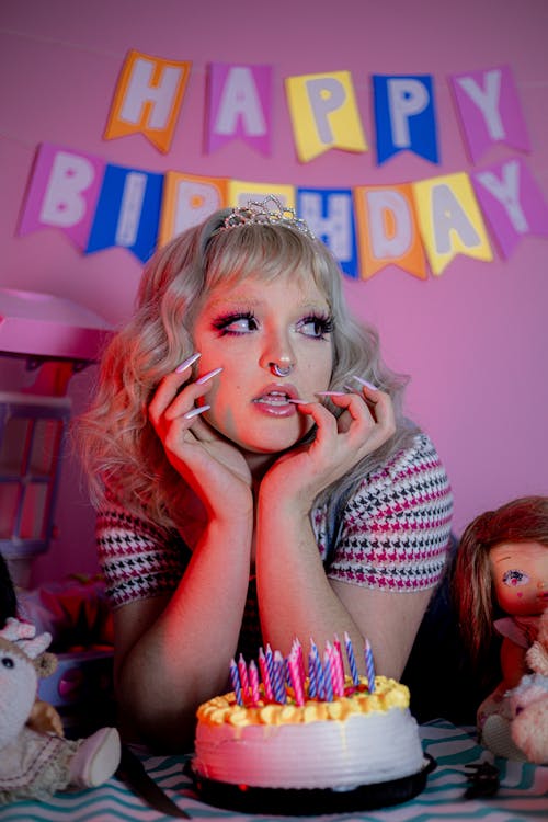 Free Young Woman Lying with a Birthday Cake and a "Happy Birthday" Sign in the Background  Stock Photo