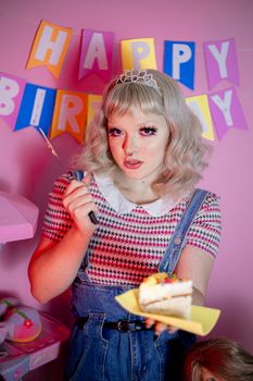 A young woman in a festive setting holding a piece of cake with birthday decorations.