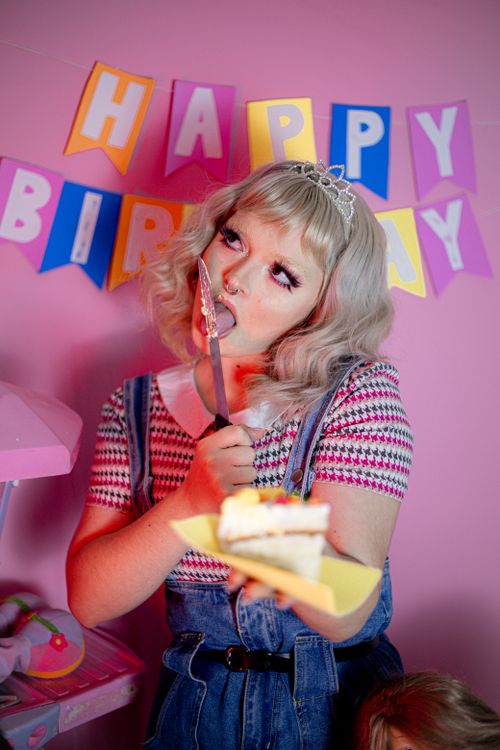 Free Woman enjoying a birthday cake slice with a playful expression in front of festive banners. Stock Photo