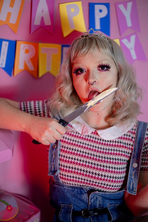 Free Unconventional birthday party featuring a woman playfully licking a knife with cake icing. Stock Photo