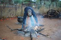 A man in rural Botswana tends to a small outdoor fire, surrounded by natural elements.