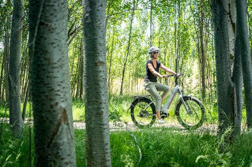 A Woman Wearing White Helmet Biking Between Green Trees