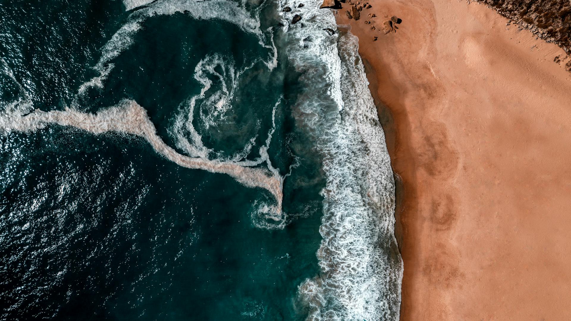 Stunning aerial view of Nazaré beach with crashing waves and sandy shore in Portugal.