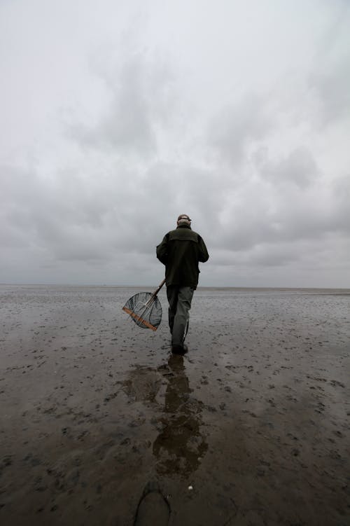 Back View of a Man Holding a Fishing Net Walking on a Beach 