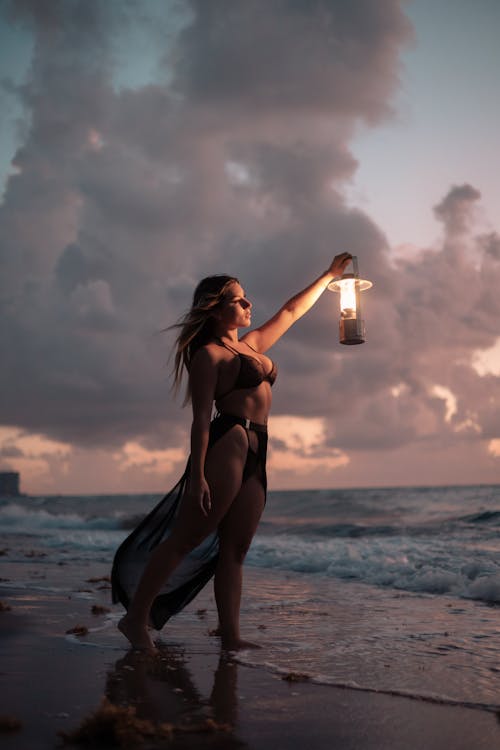 Woman with Lantern on Beach on Sunset