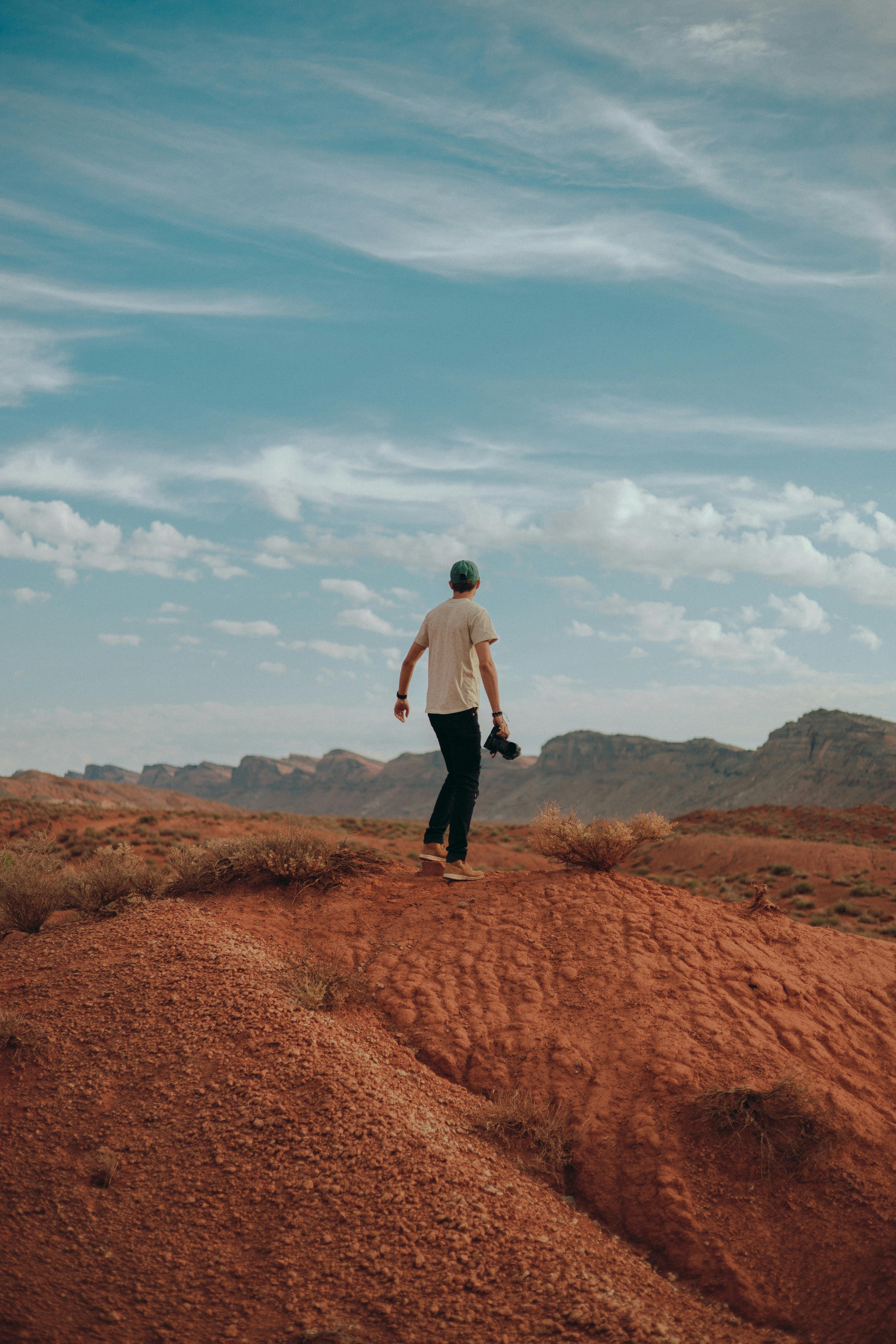 Man exploring an arid desert terrain with a camera, embracing adventure and wanderlust.