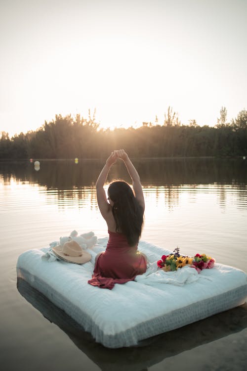 Woman in Red Dress Sitting on Mattress on the Lake