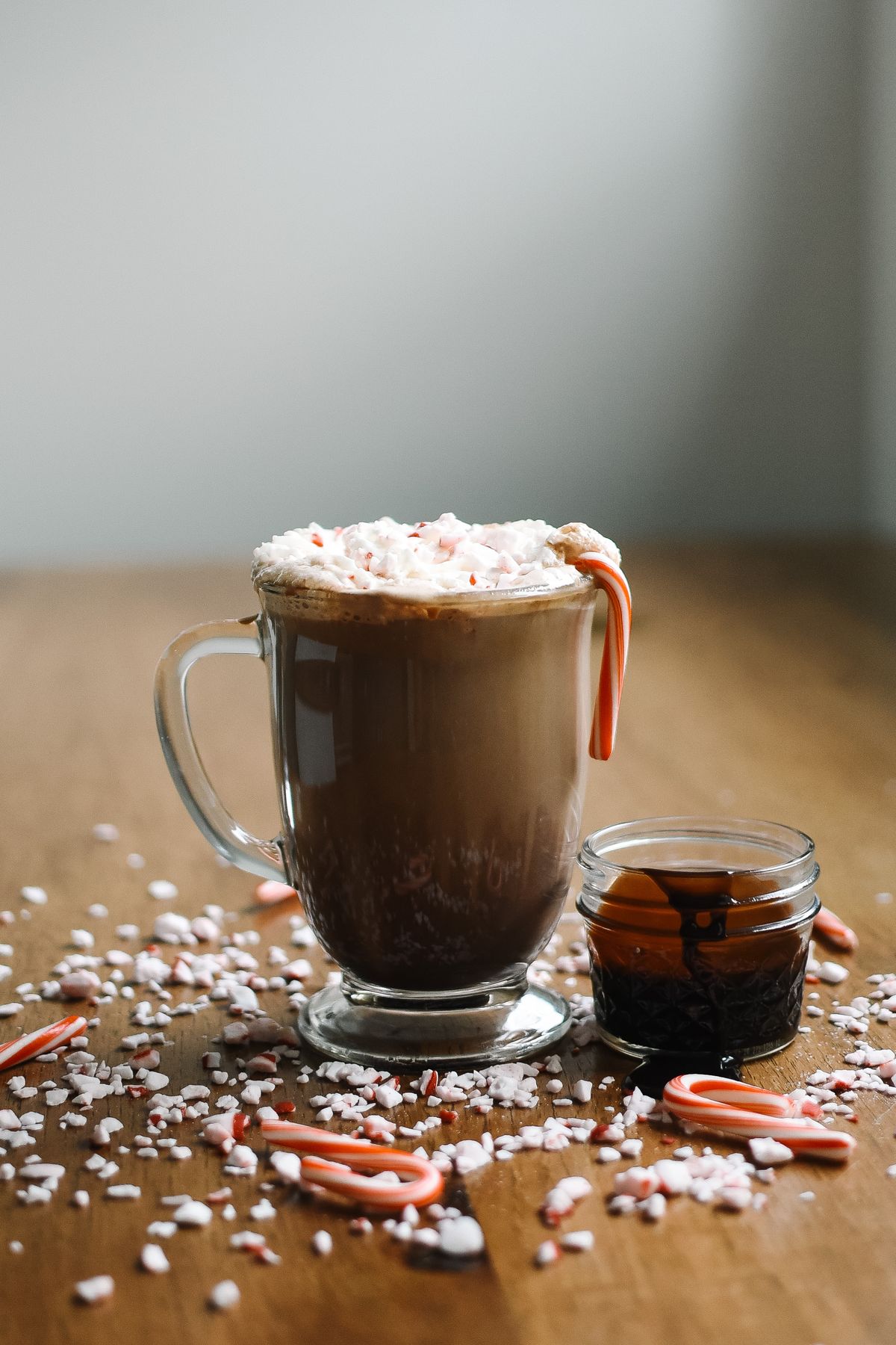 Glass mug of hot chocolate with whipped cream and a candy cane on a rustic wooden table