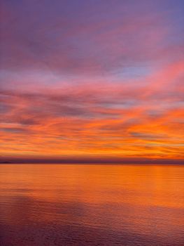 Vibrant sunset over the sea in Lezhë, Albania, with warm orange and pink hues reflecting on the water.