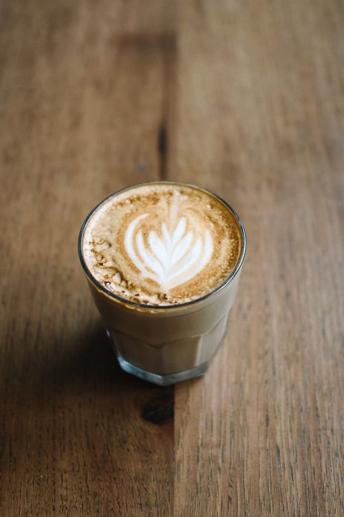 Free A vertical shot of a latte with intricate art, served in a glass on a wooden table. Stock Photo