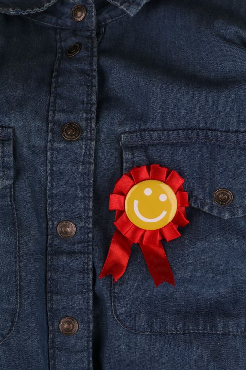 Free Close-up of a denim shirt pocket with a red ribbon and smiley badge on it. Stock Photo