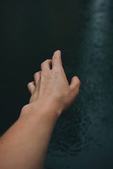 Wet hand reaching out in a close-up shot with a dark background, creating a moody atmosphere.