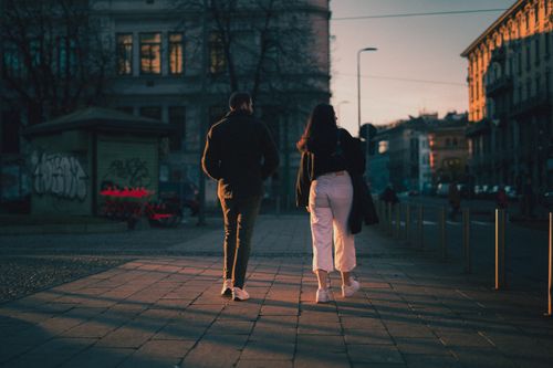 Free A man and woman walking down a city street during sunset, capturing urban life. Stock Photo