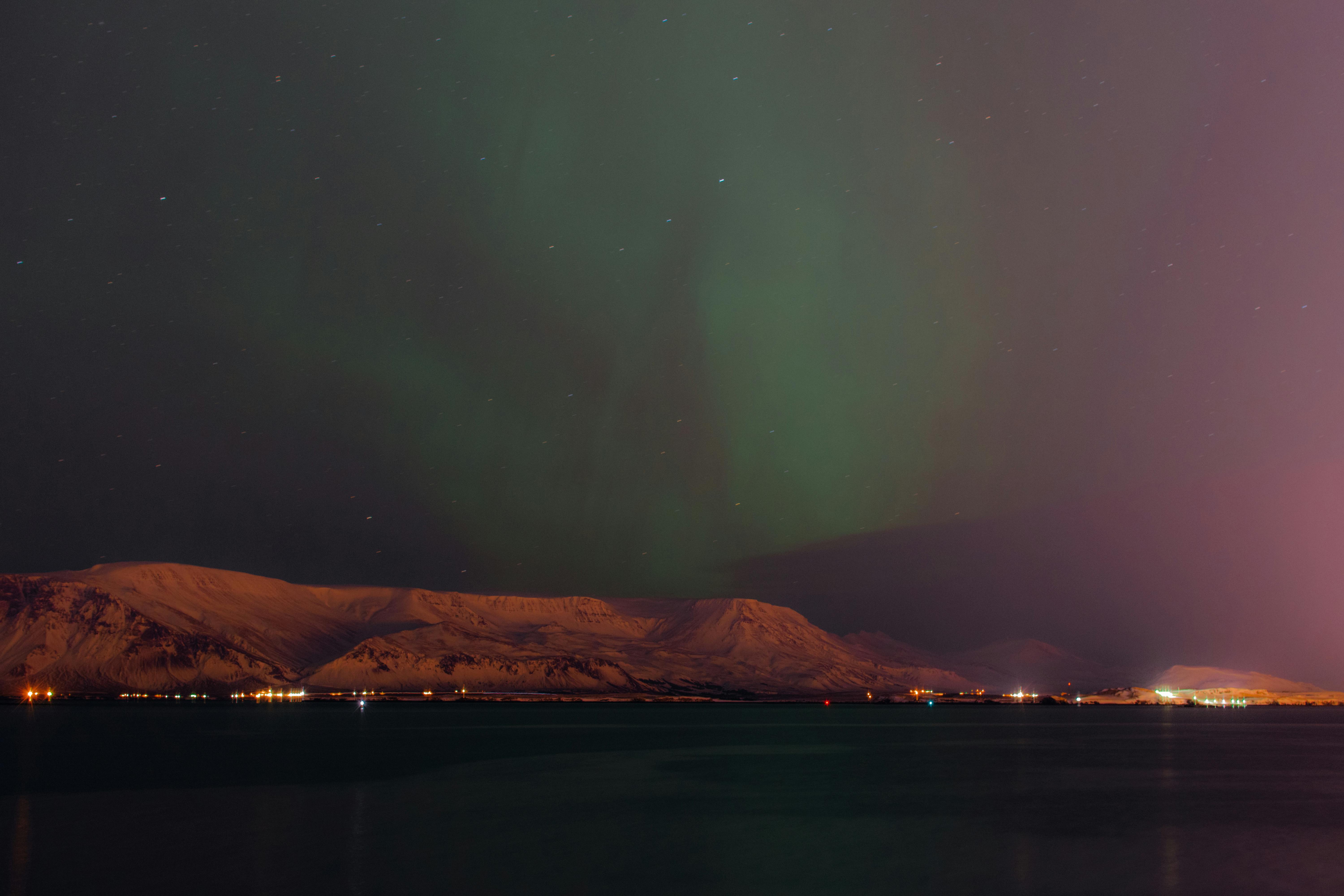 迷人的北极光映照在宁静湖泊旁白雪覆盖的山脉上，形成令人惊叹的夜间景观