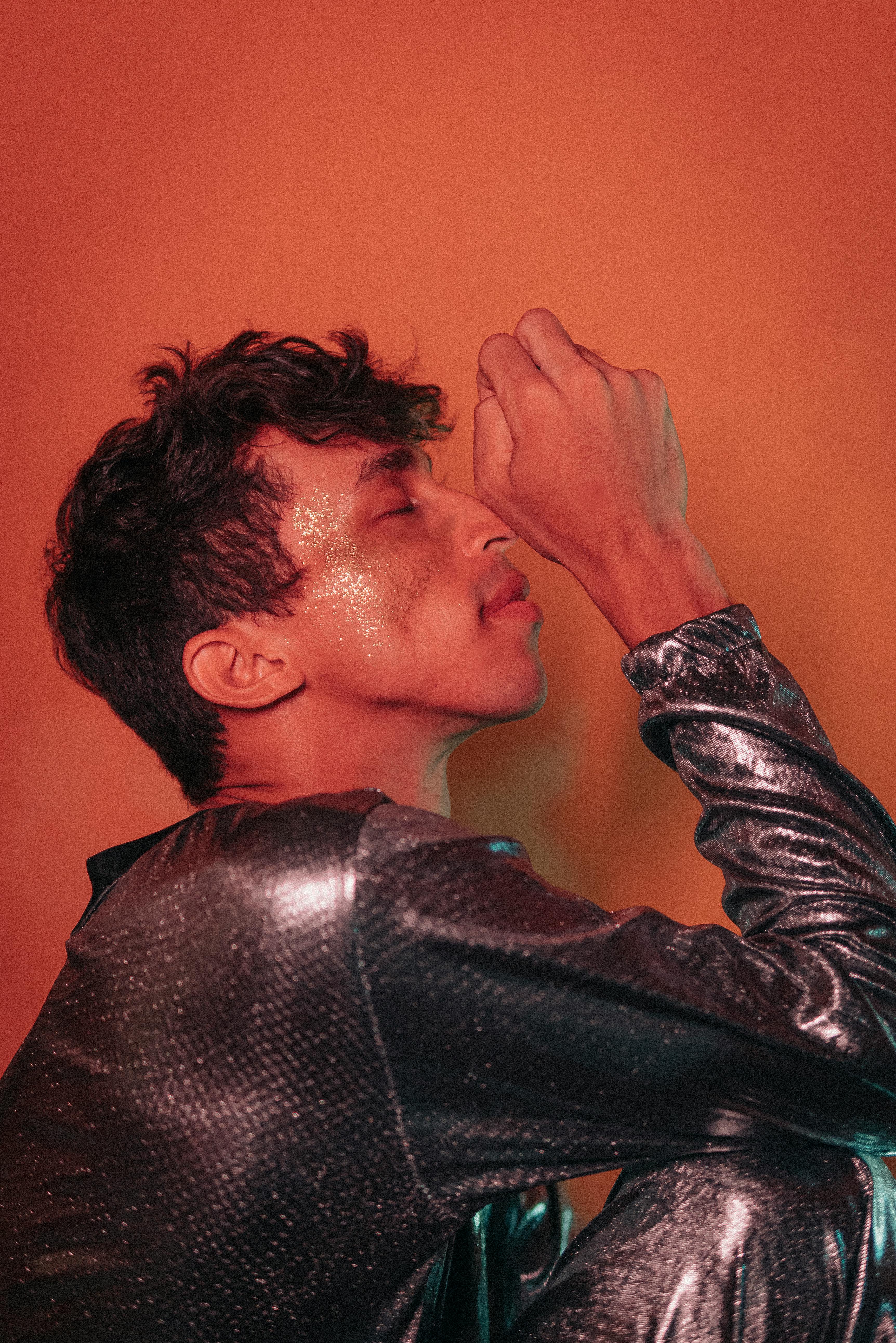 Stylish portrait of a man in a glittery outfit with a vibrant background, embracing modern fashion.