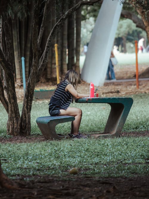 Free Woman Sitting at a Concrete Table in a Park  Stock Photo