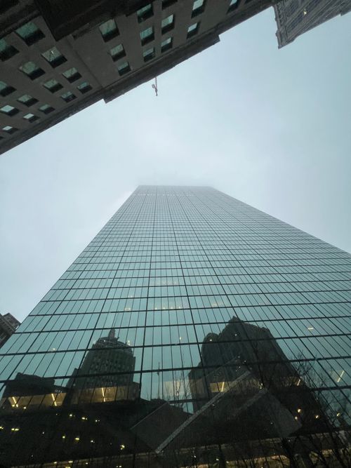 Free A dramatic perspective of a skyscraper reaching into the cloudy sky, reflecting surrounding buildings. Stock Photo