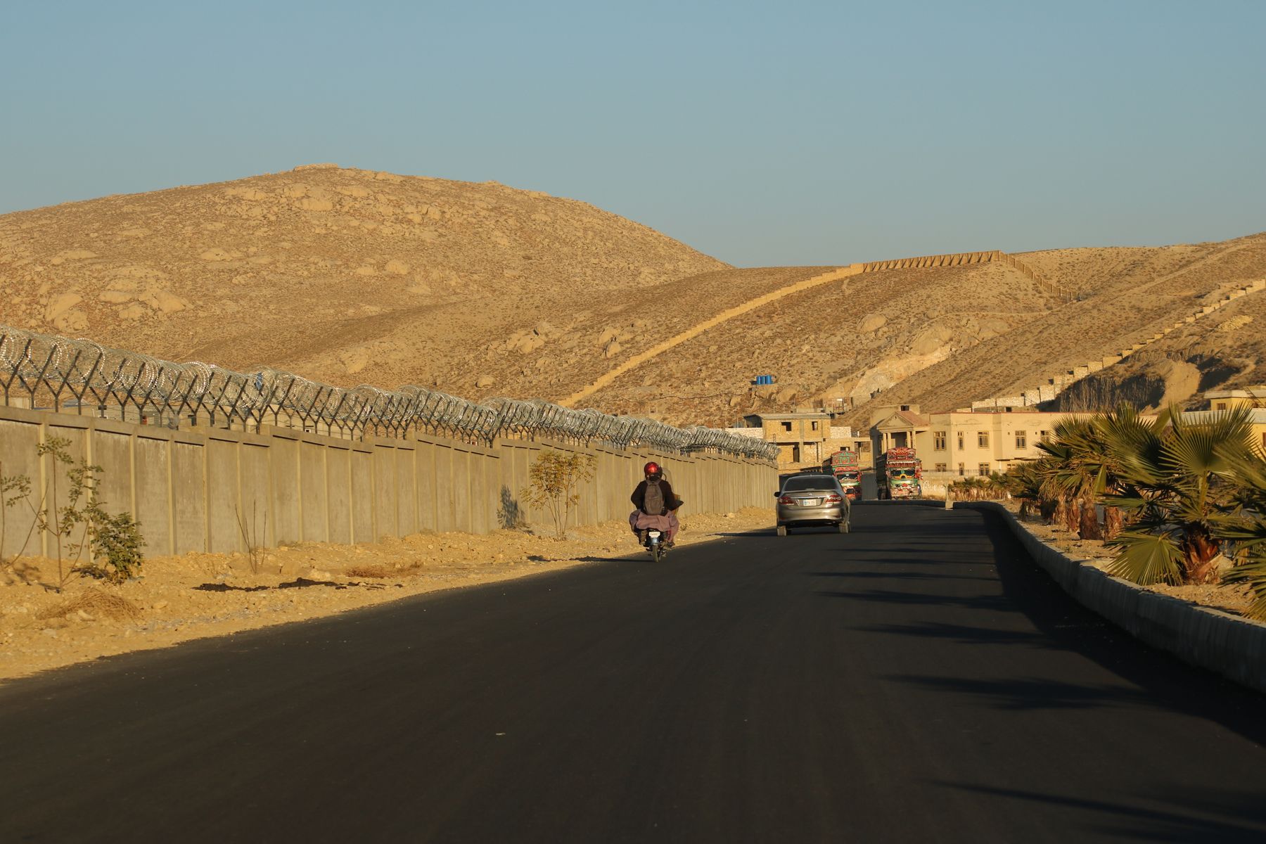 A motorcyclist rides along a road in Quetta, surrounded by desert landscape and walls.