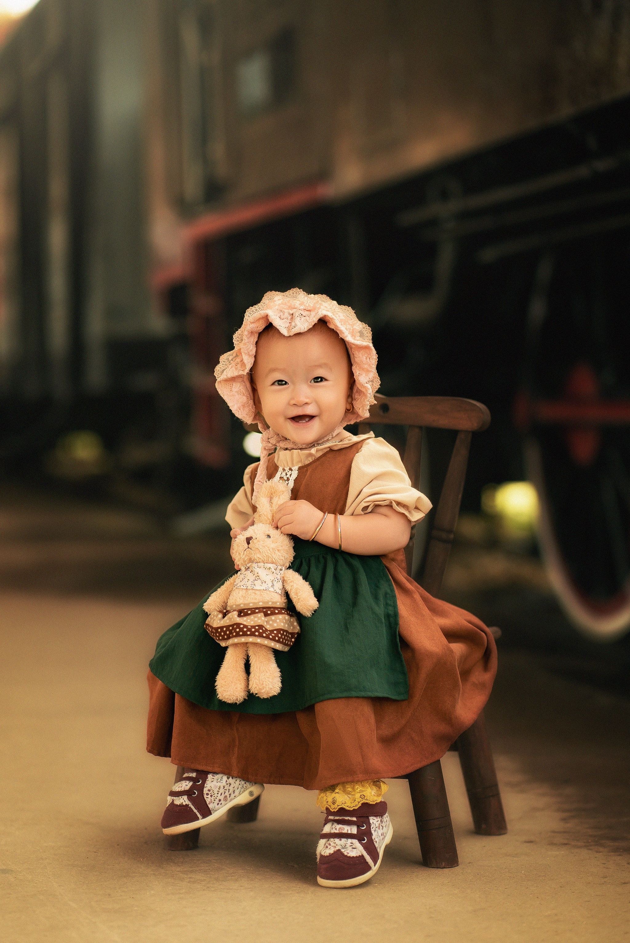 Adorable child in vintage attire sitting happily with a stuffed toy, capturing innocence.