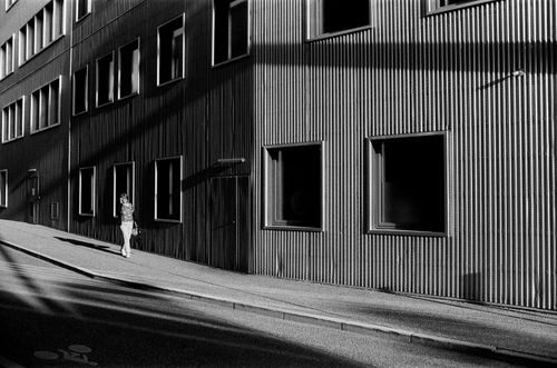 Free Black and white photo of a modern building facade lit by sunlight and a woman walking on the sidewalk in Nancy, France. Stock Photo
