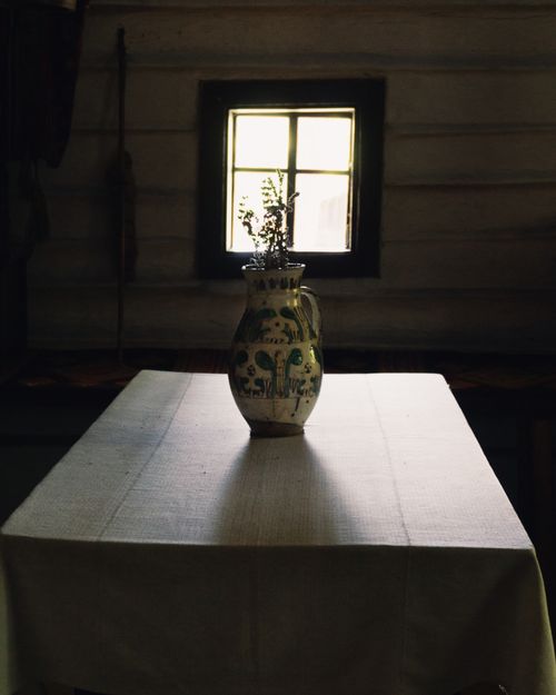 Free A decorative vase sits on a rustic wooden table against a window in a dimly lit room, creating a vintage atmosphere. Stock Photo