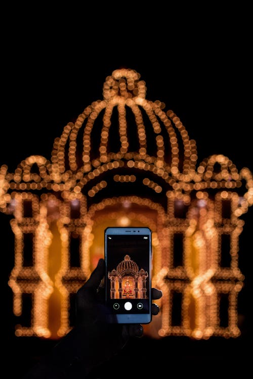 Person Taking Photo of String Light Decor With Smartphone during Nighttime