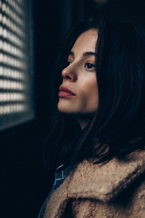 Free A thoughtful woman gazes out a grated window, wrapped in a warm coat. Stock Photo