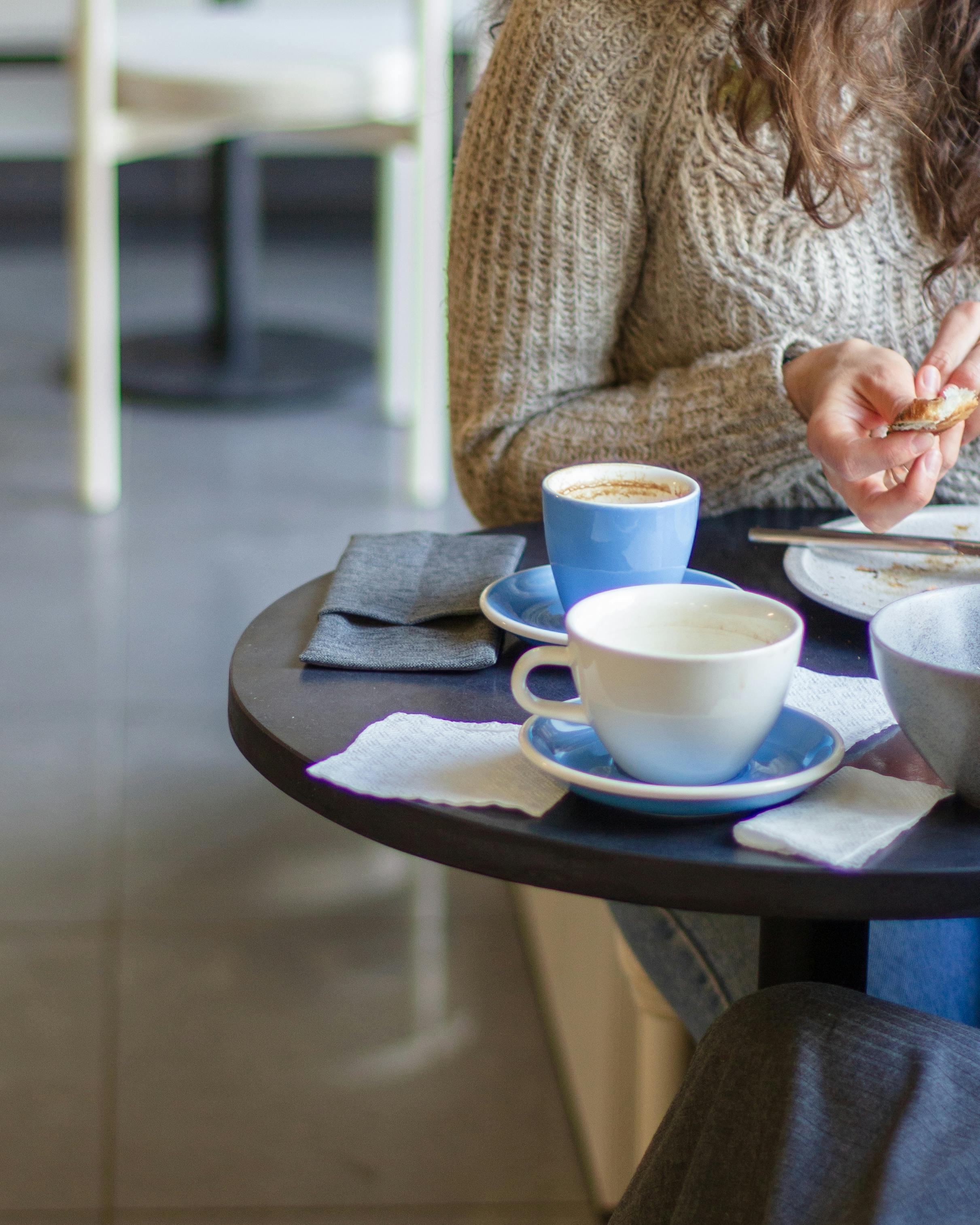 A cozy coffee shop ambiance with a woman in a sweater enjoying her drink at a table.