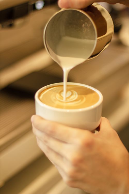 Free Close-up of a barista pouring milk to create latte art in a cappuccino indoors. Stock Photo