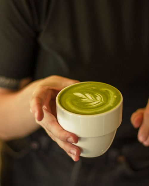 Free Detailed shot of a hand holding a matcha latte with intricate latte art, indoors. Stock Photo