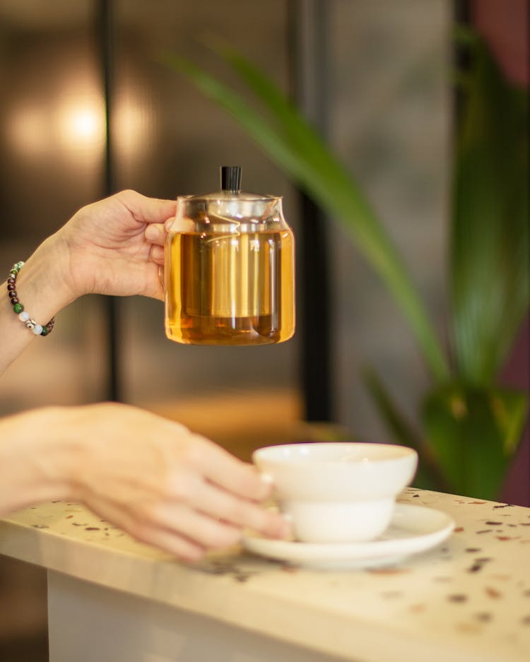 A Person Holding A Tea Pot And A Ceramic Cup