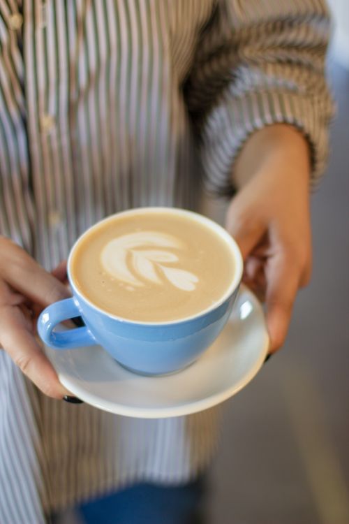 Free A person holding a latte with art in a blue cup, creating a cozy vibe. Stock Photo